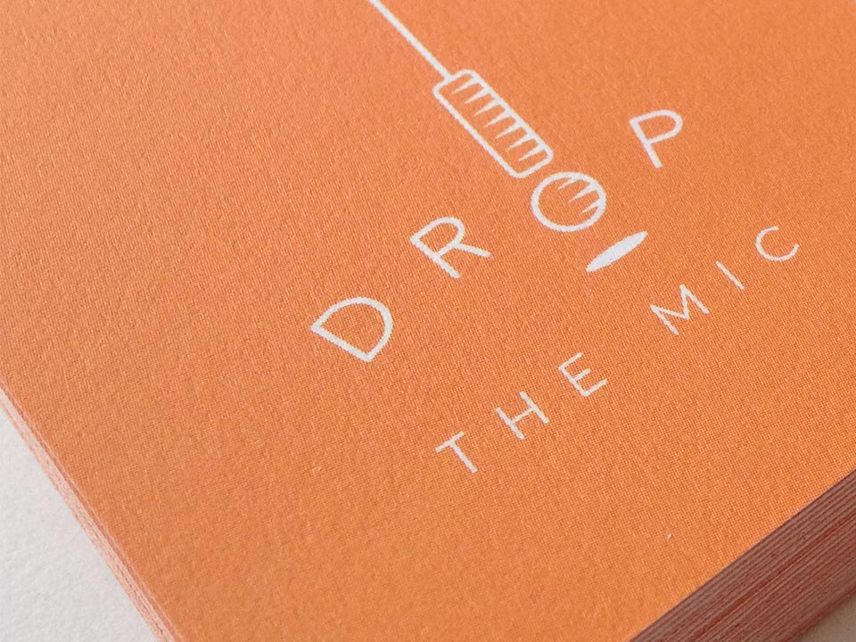 A close up of a business card featuring the Drop The Mic logo designed by Ashley Spencer